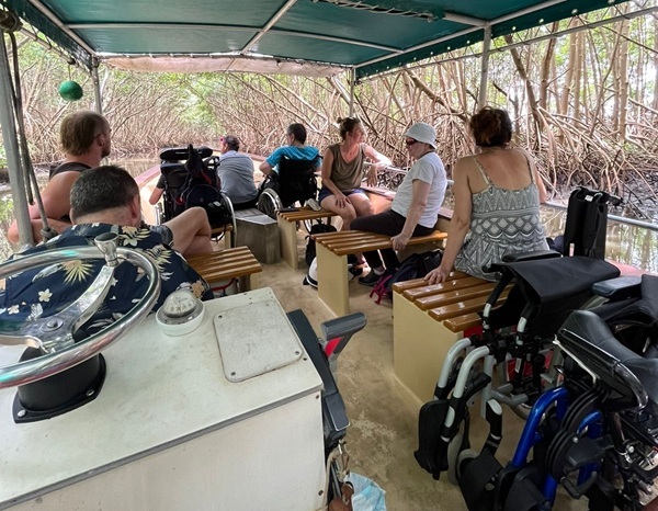 Inside of the boat in the middle of a tour with two people in wheelchairs at the front and two folded wheelchairs at the back.